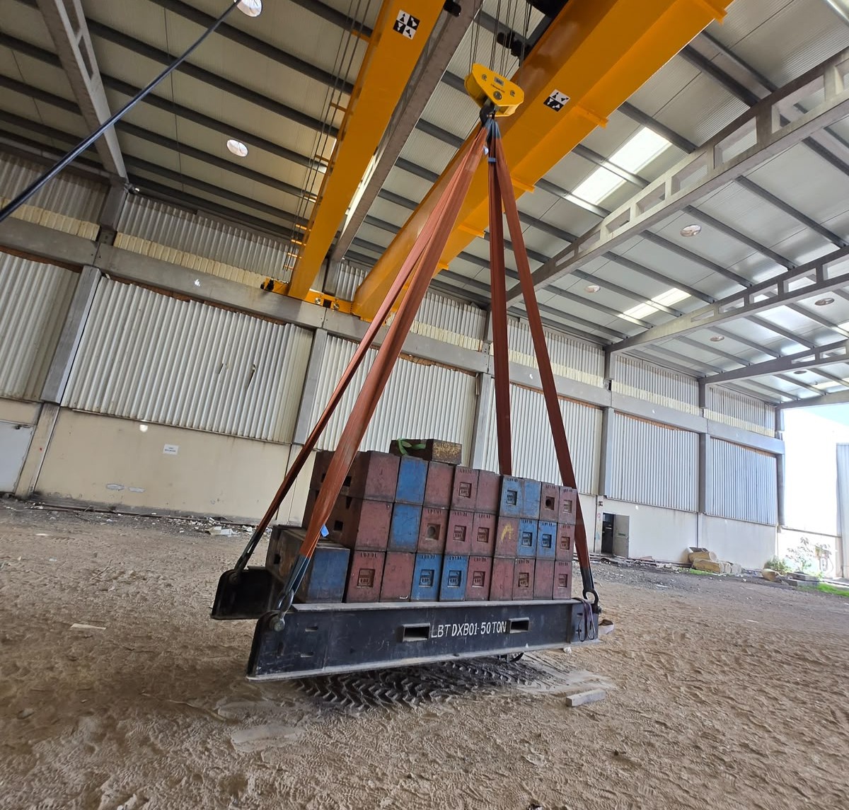 Stacked heavy-duty test weight blocks rigged beneath an overhead crane hook